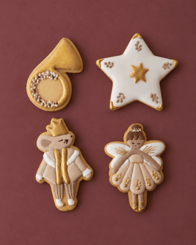 Biscuiți artizanali de Crăciun The Nutcracker: corn auriu, stea albă, șoricel cu coroană și balerină cu aripi, pe fundal vișiniu.